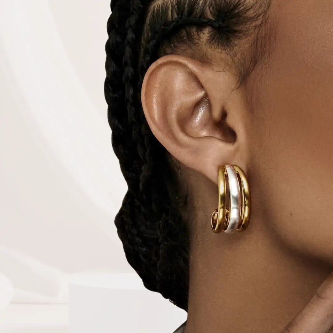 Close-up of an ear wearing a gold hoop earring with a braided hairstyle.